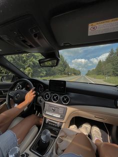 a person driving a car on a road with trees in the background and clouds in the sky