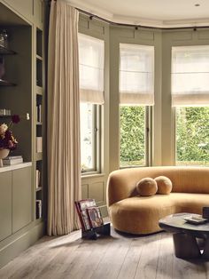 a living room filled with furniture and windows covered in draping next to bookshelves