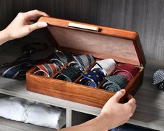 a wooden box filled with lots of ties on top of a table next to a person's hand