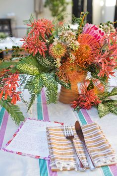 an arrangement of flowers on a table with napkins and utensils next to it