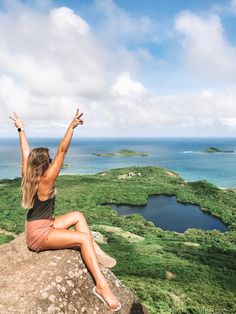 a woman sitting on top of a large rock with her arms up in the air