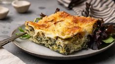 a white plate topped with lasagna covered in cheese and spinach next to a fork