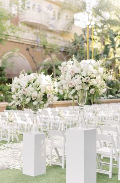 two vases filled with white flowers sitting on top of a grass covered field next to chairs