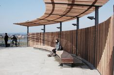 a woman sitting on top of a wooden bench next to a bike parked in front of a fence