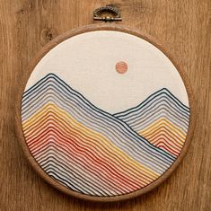 an embroidery project with mountains and sun in the background on a wooden hoop hanging on a wall