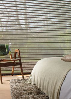 a bed sitting next to a window with blinds on it's side and a chair in the foreground