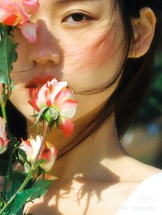 a woman with flowers in her hair looking at the camera while she's holding it up to her face