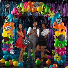 two women and a man standing in front of a backdrop with balloons, streamers and decorations