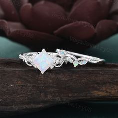 an opal and diamond ring sits on a piece of wood next to a flower