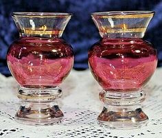 two pink glass vases sitting on top of a white doily covered tablecloth