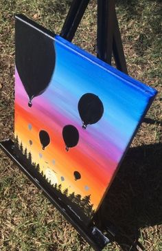 an easel with a painting on it that looks like hot air balloons floating in the sky