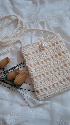 a crocheted purse sitting on top of a white bed next to dried flowers