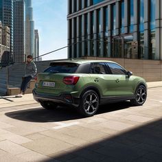 the rear end of a green suv parked in front of a tall building on a city street