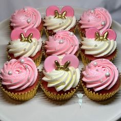 cupcakes with pink frosting and gold decorations on a white cake platter