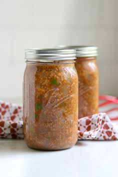 two jars filled with food sitting on top of a white counter next to a red and white napkin