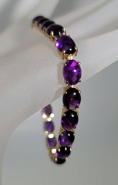 "Beautiful bracelet! Marked 14K yellow gold amethyst cabochon cut gemstone bracelet. The 14K yellow gold bracelet is set with nineteen oval shaped cabochon cut amethyst gemstones. Each amethyst measures approximately 8.00 mm x 6.50 mm for an approximate total amethyst weight set in the bracelet of 23.75 carats. The 14K yellow gold amethyst bracelet has a solid and secure 14K yellow gold clasp with a safety catch. The amethyst bracelet measures approximately 7 1/4\" inches in length. The 14K yell Formal Purple Cabochon Gemstones, Elegant Cabochon Amethyst Gemstones, Elegant Amethyst Cabochon Gemstones, Formal Purple Oval Cabochon Jewelry, Oval Cabochon Bracelet In Fine Jewelry Style, Yellow Gold Amethyst Gemstone Bracelets, Yellow Gold Bracelets With Amethyst Gemstone, Oval Cabochon Bracelet Fine Jewelry, Yellow Gold Amethyst Bracelets With Gemstone