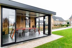 a glass walled dining area with chairs and tables in the grass outside an extension to a house