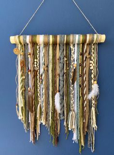 a wall hanging made out of different colored ropes and feathers on a blue wall with a string