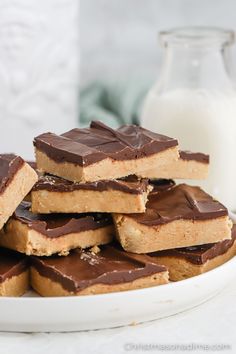 a white plate topped with pieces of chocolate covered peanut butter bars next to a glass of milk