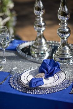 the table is set with silver and blue place settings, napkins, and wine glasses