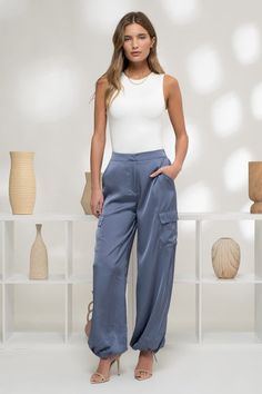 Elevate your style with our Denim Blue Satin Cargo Jogger Pants. The high waist and elasticized back provide a comfortable fit, while the hook and bar closure and zipper ensure a secure closure. Featuring multiple pockets and a drawstring cuff with stopper, these jogger pants offer a sleek satin texture and lightweight feel for versatile wear. Fabric & fit: 100% polyester Model is wearing size small. Blue Jogger Pants Outfit, Silk Cargo Joggers Outfit, Chic Blue Satin Bottoms, Silk Cargo Pants Outfit, Blue Cargo Lounge Bottoms, Satin Joggers Outfit, Blue Satin Pants, Satin Jogger Pant, Blue Cargo Pants Outfit