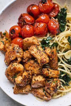 a white bowl filled with pasta, chicken and cherry tomatoes next to spinach leaves