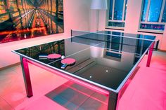 a ping pong table in a room with pink lighting on the floor and paintings behind it