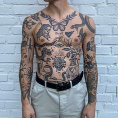 a man with tattoos standing in front of a brick wall