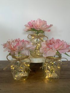 pink flowers are in mason jars with string lights on the top and bottom, sitting on a wooden table