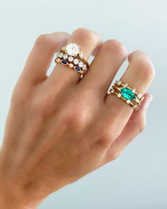 a woman's hand holding two rings with emeralds and blue stones on them