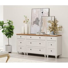 a white dresser with drawers and pictures on it in a room next to a potted plant