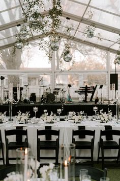 the tables are set with white flowers and candles for an elegant wedding reception in a tented area