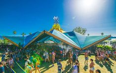 a large group of people standing around in front of a blue tent and some trees