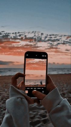 a person taking a photo with their cell phone on the beach at sunset or sunrise