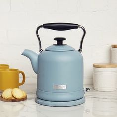 a blue tea kettle sitting on top of a counter next to two yellow mugs