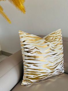 a white and gold pillow sitting on top of a brown couch next to a yellow feather