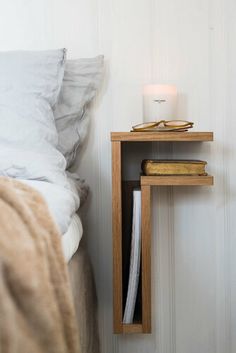 a bedside table with a candle on it next to a white wall and a bed