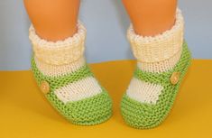 a doll's legs wearing green and white knitted slippers with buttons on them