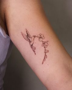 a woman's arm with a humming bird and flower tattoo on the left arm