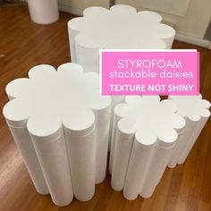 three white vases with flowers on them sitting on a wooden floor next to a pink sign that says, styrofoam stackable daisies texture not shiny