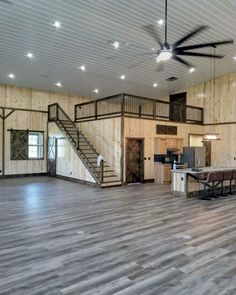 an empty living room with wood floors and ceiling fan in the center, stairs leading up to second floor