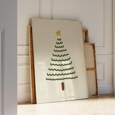 a framed christmas tree on the floor in front of a white wall and wooden shelves