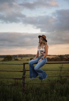 a woman sitting on top of a wooden fence next to a green grass covered field