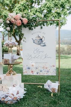 a welcome sign with teapots and flowers on it is sitting in the grass