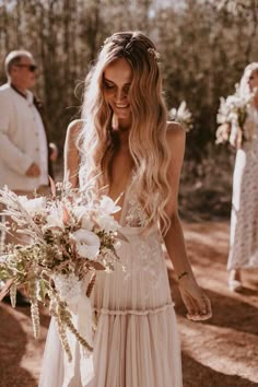 a woman in a wedding dress holding a bouquet and looking down at her phone screen