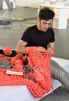 a man sitting on top of a table next to an orange crocheted blanket