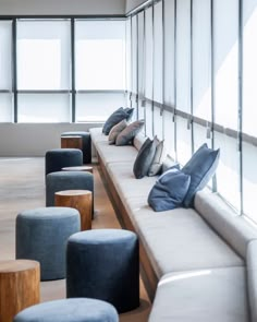 a long bench with many pillows on it in front of large windows and wooden stools