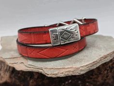 two red leather bracelets sitting on top of a rock