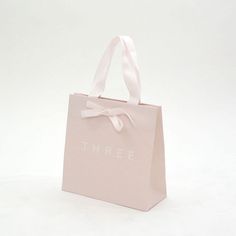 a pink shopping bag with the word three printed on it and a bow at the top