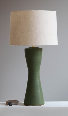 a green table lamp sitting on top of a white shelf next to a light bulb